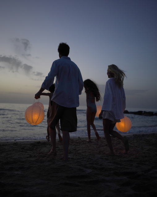 A family walking along the beach at dusk, carrying lanterns