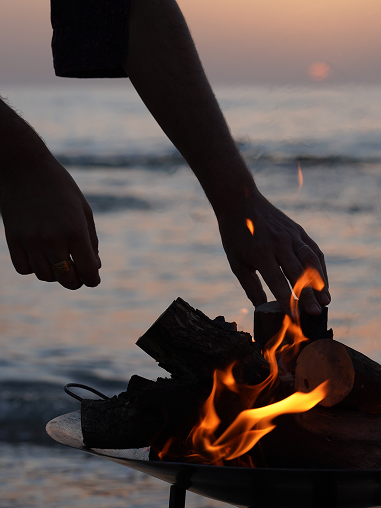 Hands warming over a beach bonfire at sunset